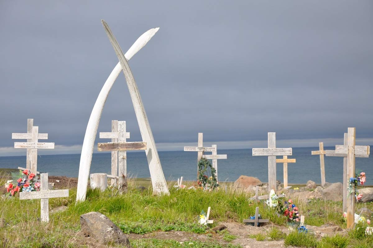 A cluster of wooden crosses and flowers on grassy ground, overlooking the ocean