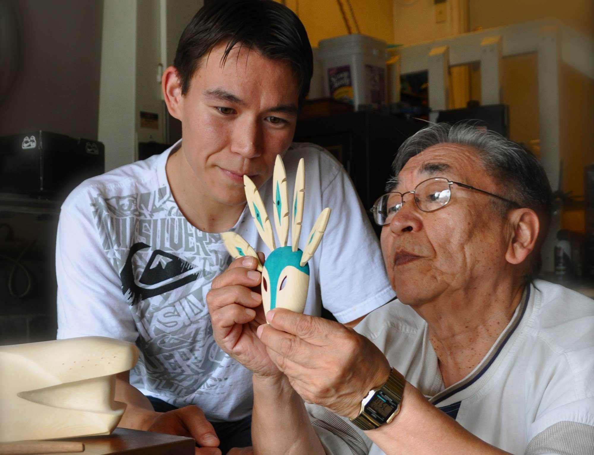 two people, one older, one younger, making a small mask with sculpted feathers